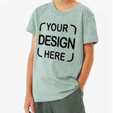 A person wearing a light sage green heathered t-shirt with black placeholder text reading 'YOUR DESIGN HERE' on the front